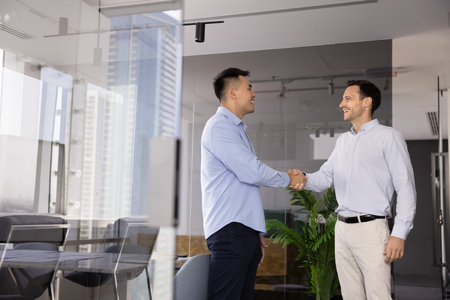 Partnership agreement. Happy confident diverse male entrepreneurs coworkers standing in bright glass...