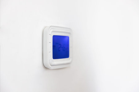 Wall mounted panel of digital thermostat with blue backlit screen. Gadget for regulating temperature...