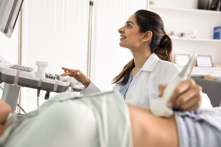 Smiling Indian female doctor ultrasonographer performing ultrasound scan on woman patients abdomen...