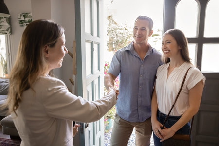 Realtor handshake with smiling couple, greeting, standing in house entrance, starting meeting of...