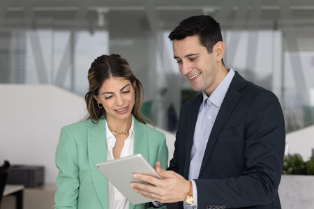 Two diverse Hispanic corporate workers colleagues engaged in professional teamwork using tablet...