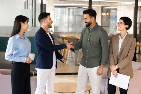 Smiling multiethnic business partners, team members shaking hands after successful negotiation in...