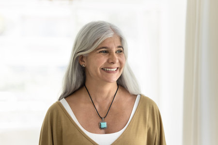 Middle-aged woman dressed in casual clothes looking with smile into distance, standing alone in...