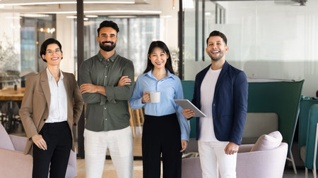 Multiethnic business team standing in corporate office, smiling, looking at camera, posing for...