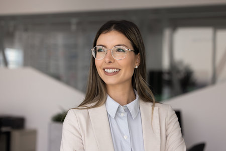 Head shot portrait of confident young Hispanic businesswoman standing alone in modern office, looks...