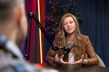 Woman host speaking into microphone during podcast interview, recording digital content for audio...