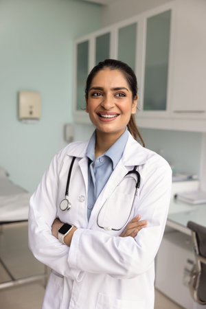Portrait of motivated woman doctor in coat stand in examination room, looks away with contented...
