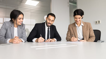 Diverse smiling businesspeople sitting at conference table signing legal contract documents,...