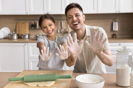 Cheery girl and father having fun while cooking pastries in modern kitchen on weekend at home,...