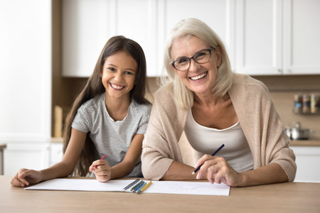 Portrait of senior granny and little cute granddaughter drawing pictures with colored pencils, spend...
