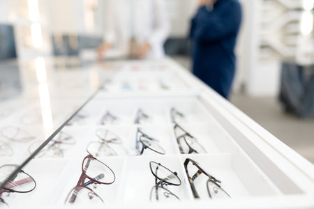 Closeup optical shop display diverse eyeglasses frames arranged on shelves, blurred showroom background, stylish glasses selection, vision correction, fashion accessory, professional ophthalmic retail