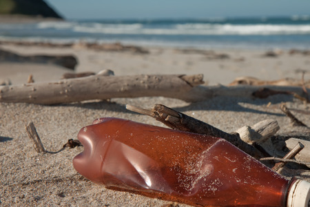 littered bottle lying among storm debris on a sandy beach の写真素材