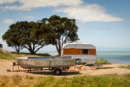 New Zealand summer camping scene caravan and aluminium fishing boat beside a beach with Pohutukawa trees in the backgroundの写真素材