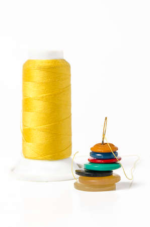 Yellow thread with needle and buttons on white background