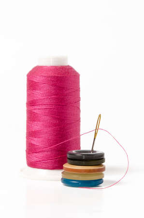 Pink thread with needle and buttons on white background