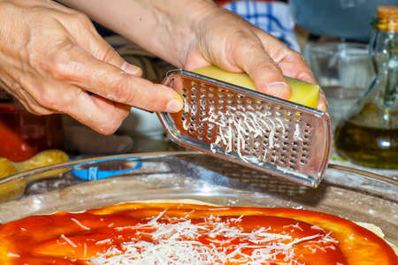 Hands on first plane using a grater, grate cheese for a pizzaの写真素材