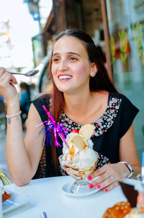 Portrait of young brunette smiling away with tasty ice cream in dessert bowl in cafeの写真素材