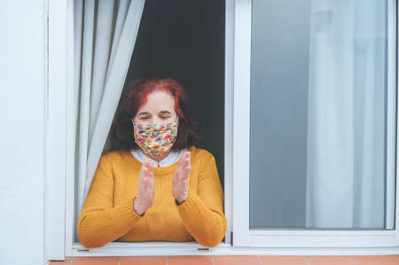 Mature woman with protective mask clapping at the window