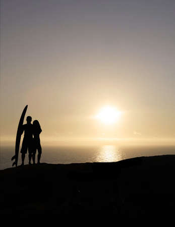 surf couple with a surf board at sunsetの写真素材