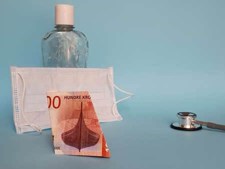 norwegian banknote of 100 kroner, face mask, bottle with gel alcohol and stethoscope on blue backgroundの写真素材