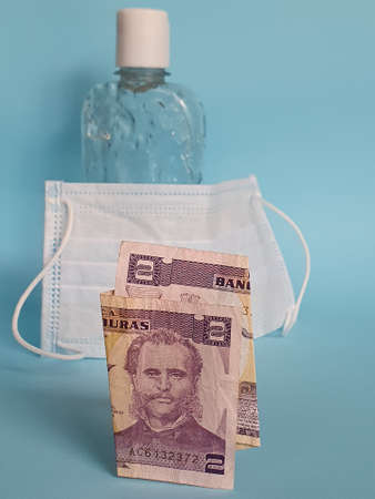 honduran banknote of two lempiras, face mask, bottle with gel alcohol and blue backgroundの写真素材