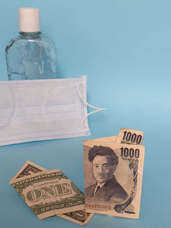 american one dollar bill, japanese banknote of 1000 yen, face mask, bottle with gel alcohol and blue backgroundの写真素材