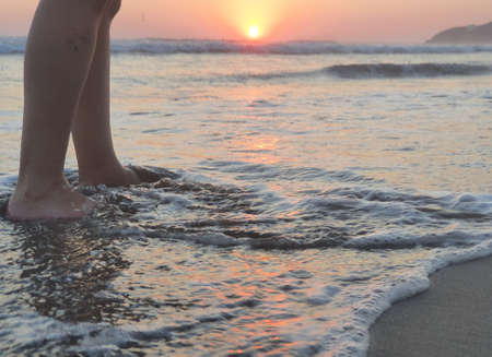 feet of a person enjoying the surf during the sunset on a beach in Acapulco, Mexico