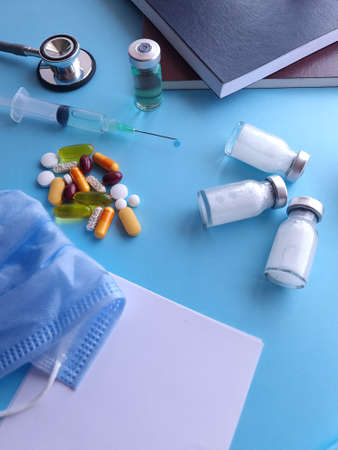 medicine bottles, syringe, pills, books, stethoscope and masks on the blue table