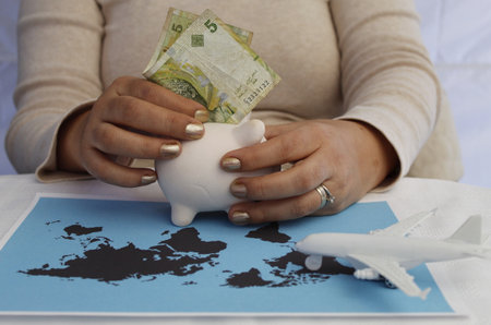hand holding Tunisian money, piggy bank and figure of an airplane on a world map