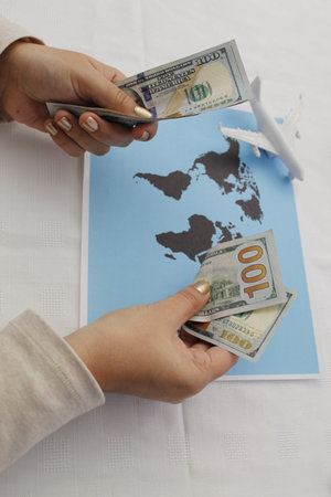 hand holding American dollar money and plastic airplane figure on a world mapの写真素材