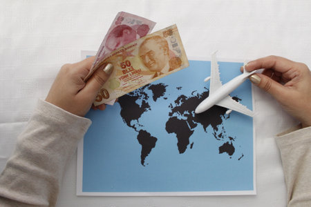 hand holding turkish money and plastic airplane figure on a world map