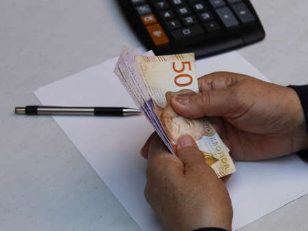 hands of a senior woman holding swedish banknotes with a pen and calculator on the table