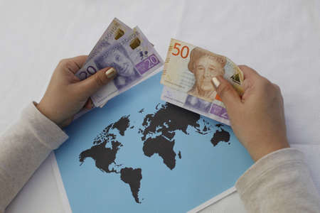 hands of a woman holding swedish money and a world map on the table
