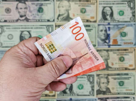 hand holding norwegian banknote of 100 kroner and background with american dollar bills