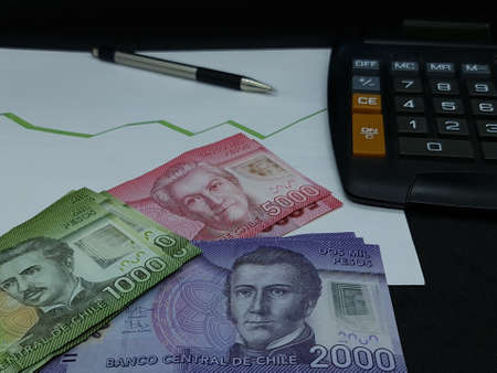 chilean banknotes, pen and calculator on background with rising trend green lineの写真素材
