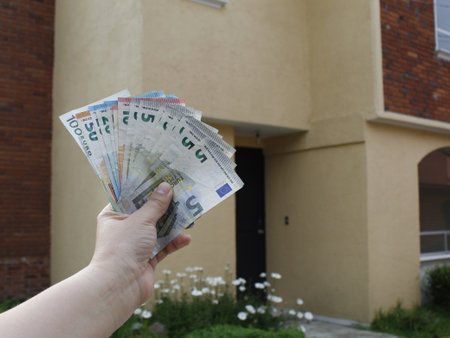 hand of a woman holding european banknotes and background with facade of a house
