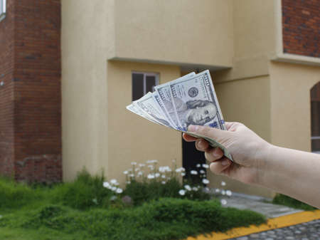 hand of a woman holding american banknotes and background with facade of a houseの写真素材