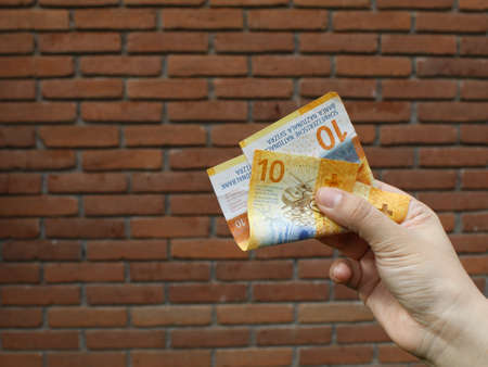 hand of a woman holding swiss banknotes and background with a brick wallの写真素材
