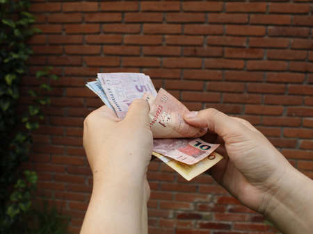 hand of a woman holding brazilian banknotes and background with a brick wallの写真素材