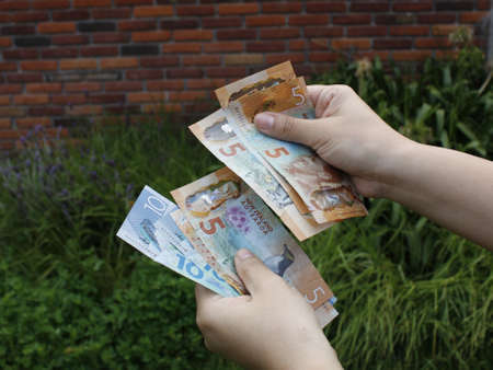 hand of a woman holding New Zealand banknotes outside a house
