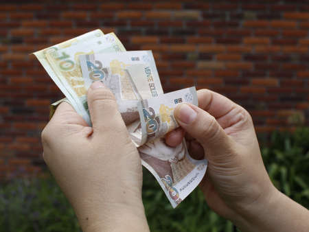 hand of a woman holding peruvian banknotes outside a house
