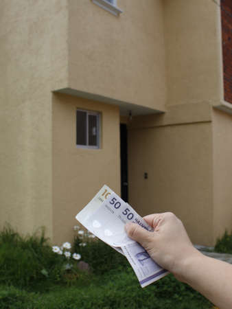 hand of a woman holding danish banknotes and background with facade of a houseの写真素材