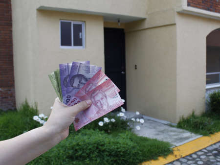 hand of a woman holding chilean banknotes and background with facade of a house
