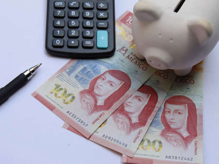 mexican banknotes of 100 pesos, piggy bank, calculator and black pen