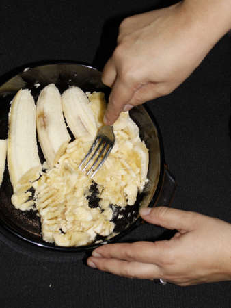 hand of a woman whipping bananas in a bowl to prepare a dessertの写真素材