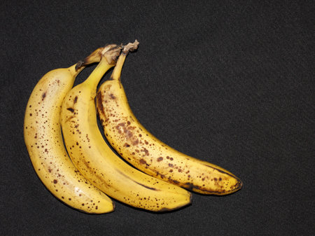three ripe bananas in a bunch on the black backgroundの写真素材