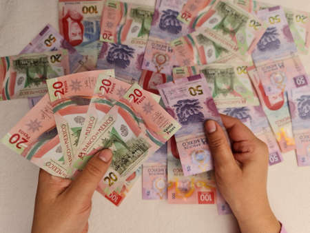 hands of a woman holding and counting mexican banknotesの写真素材