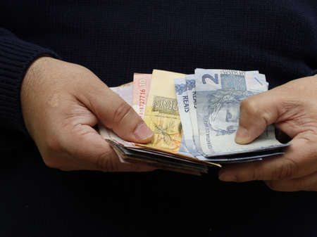hands of a man holding and counting brazilian banknotes