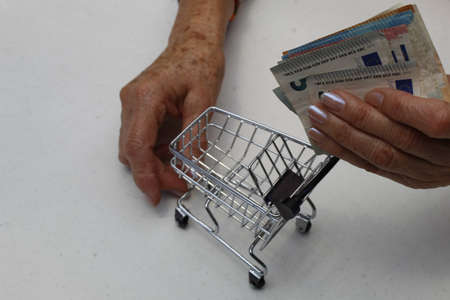 hands of an older woman holding european banknotes and shopping cart