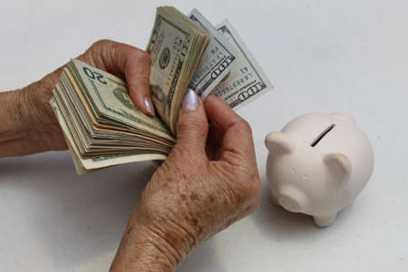 hands of an older woman holding american dollars banknotes and piggy bankの写真素材
